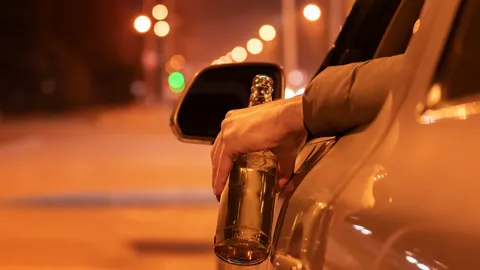 a driver holding alcohol in his hand while driving a car